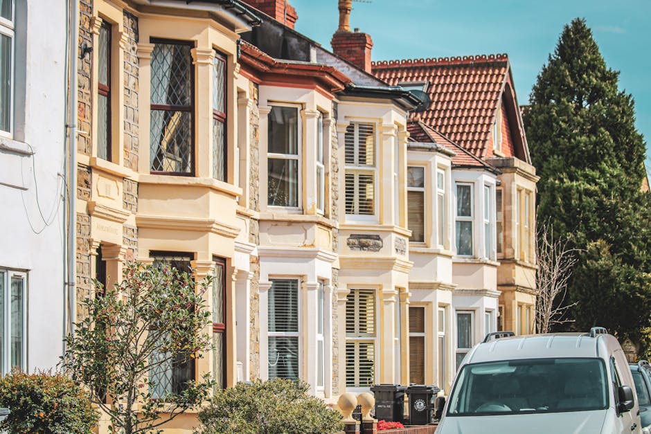 A row of Victorian terrace houses in Islington N1, featuring a variety of painted facades in shades of blue, beige, and green. The buildings are multi-storey with large sash windows, some with white d