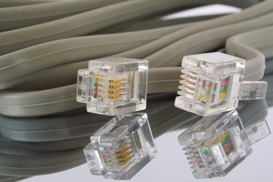 A close-up view of several clear Ethernet cables with plastic RJ45 connectors, each with gold-plated contacts and coloured wiring inside, resting on top of neatly coiled grey extension cords. The cabl
